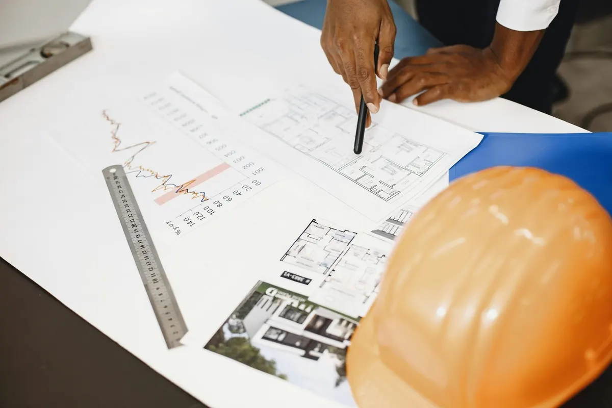 Mains annotant des plans de construction à côté d’un casque de chantier