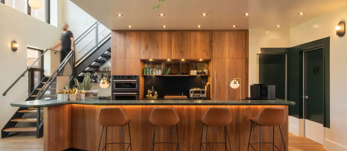 Espace commercial rénové avec comptoir en bois, tabourets et escalier vers une mezzanine